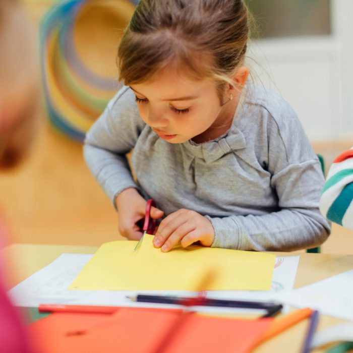 A little girl cutting some yellow craft paper