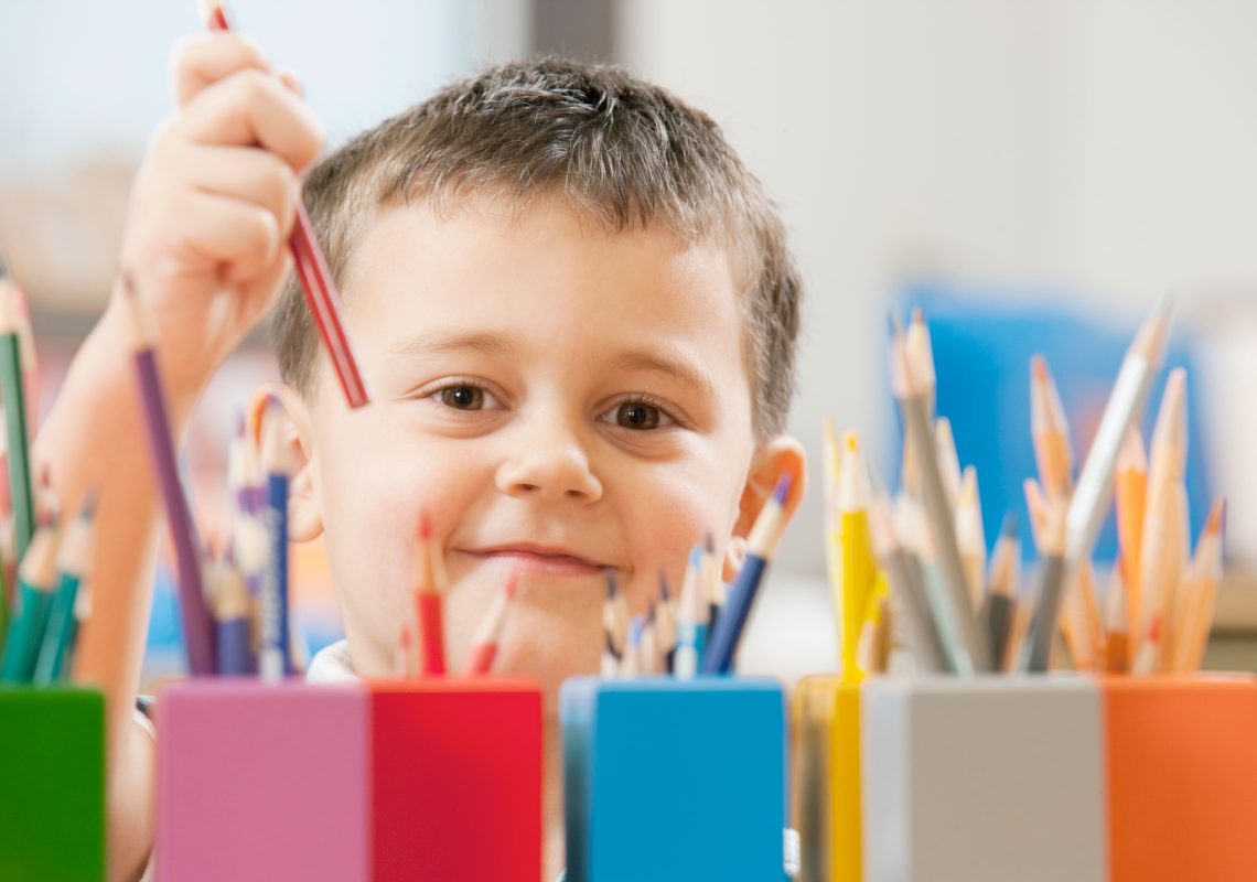 little boy picking a colored pencil from a rainbow collection of jars and pencils