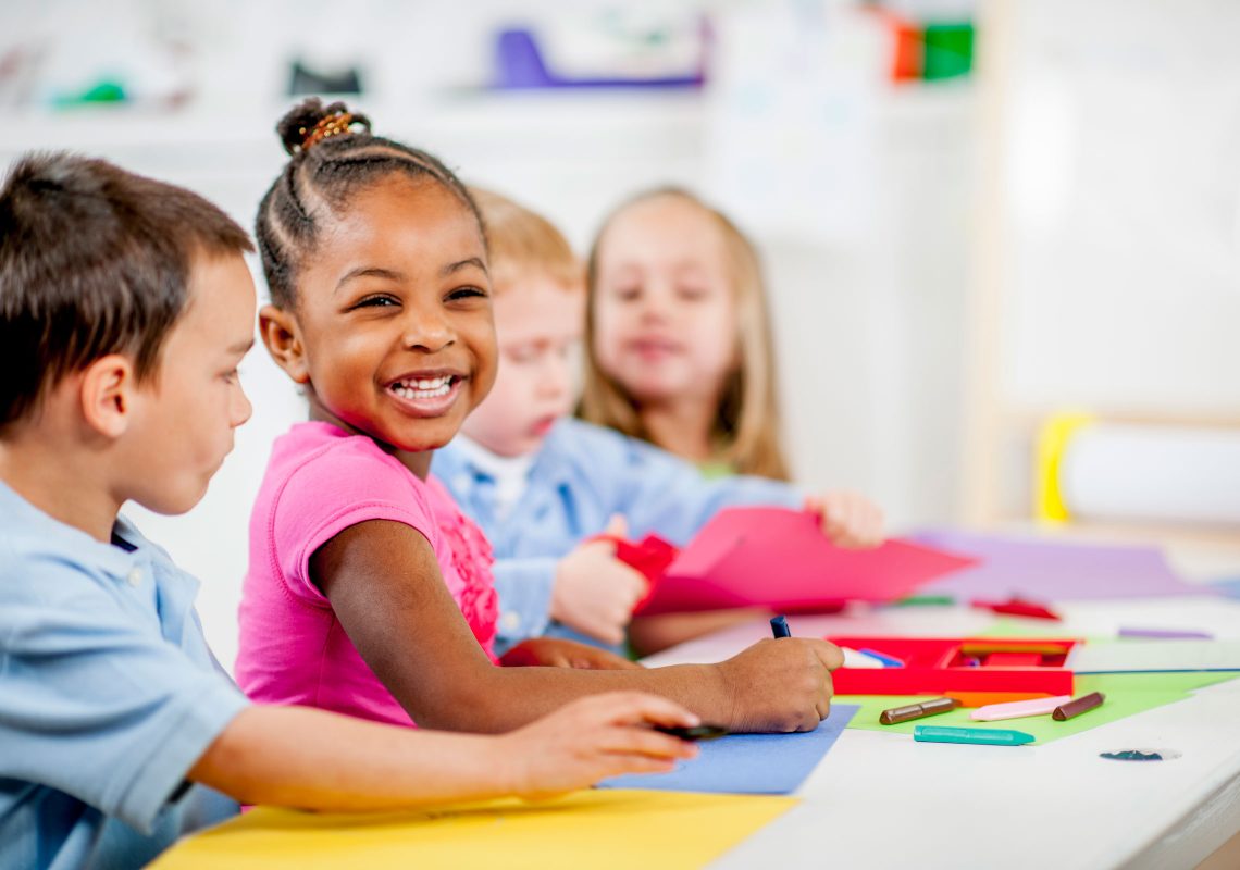 little girl smiling while coloring with crayons